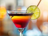 Cocktail mit Grenadine und Gin in einem eleganten Glas, garniert mit einer Zitronenscheibe und Rosmarinzweig auf einem Holztisch